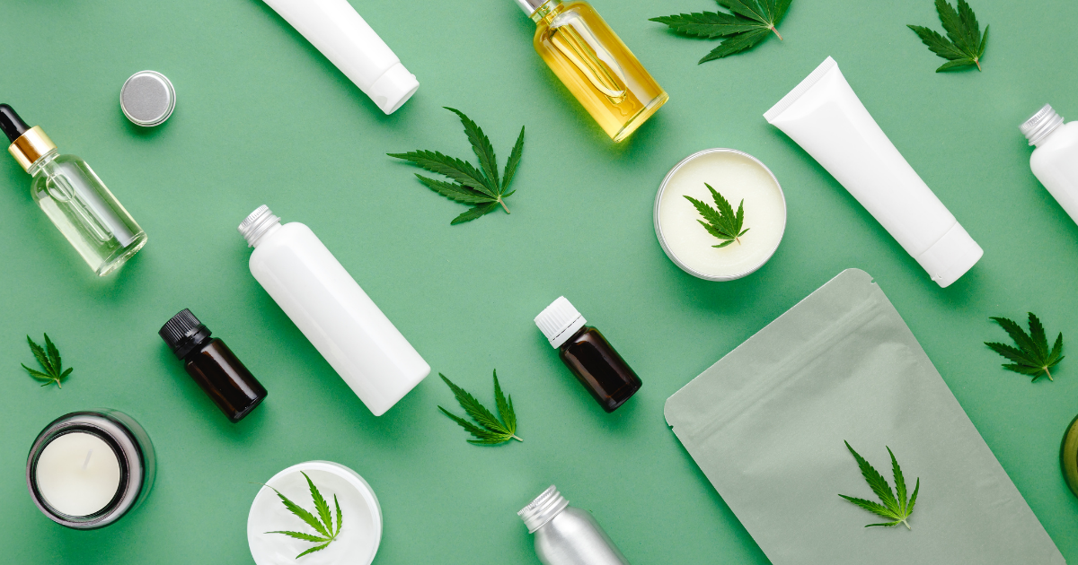 : A selection of CBD products from lotions to oils on a green surface with cannabis leaves